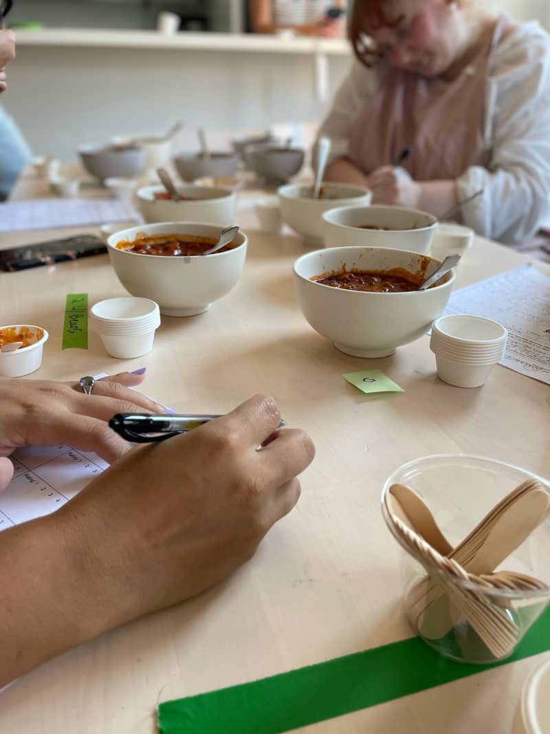 Taste testers rating bowls of canned chili on dining table.