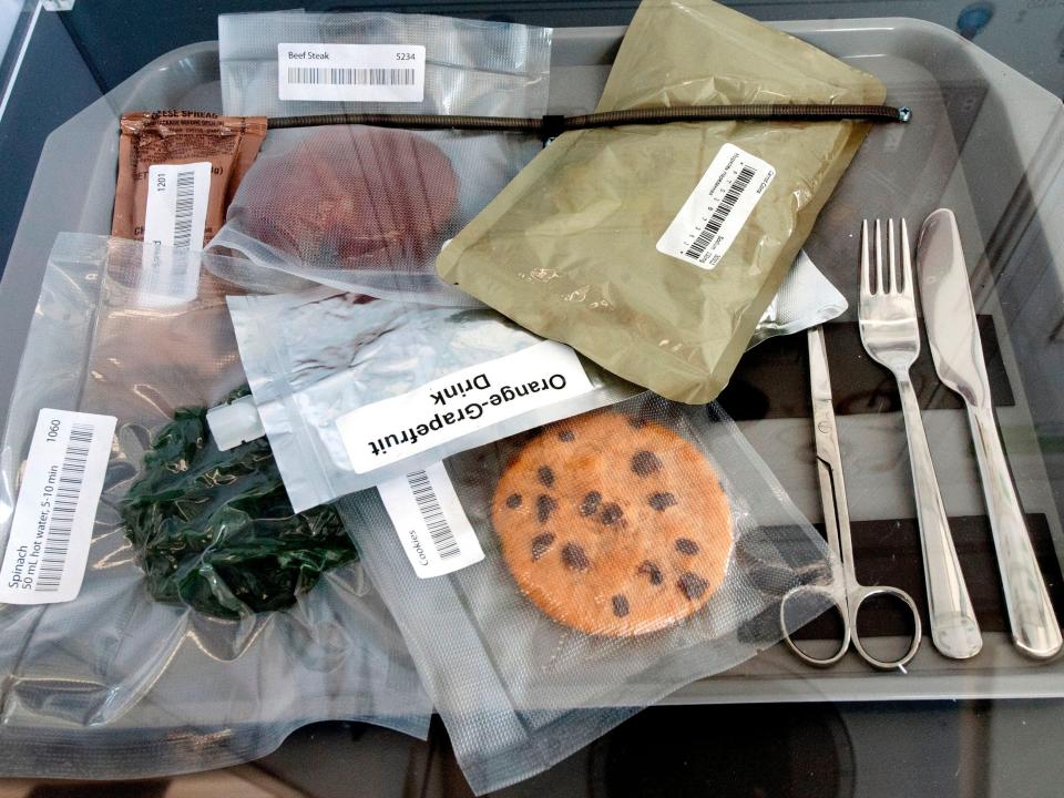 Several types of space food in clear bags and pouches, including a cookie, velcroed to a tray with utensils
