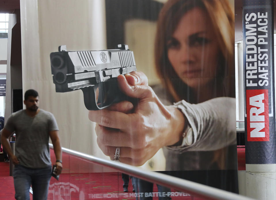 FILE - In this April 27, 2017, file photo, an attendee passes by a large banner advertising a handgun during the National Rifle Association convention at the Georgia World Congress Center in Atlanta. The National Rifle Association is gathering for its 148th annual meeting beginning Thursday, April 25, 2019, in Indianapolis. (Curtis Compton/Atlanta Journal-Constitution via AP, File)