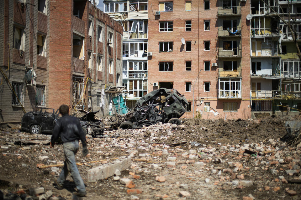 A man walks next to heavily damaged residential buildings and destroyed cars after Russian bombing in Bakhmut, eastern Ukraine, Tuesday, May 24, 2022. The town of Bakhmut has been coming under increasing artillery strikes, particularly over the last week, as Russian forces try to press forward to encircle the city of Sieverodonetsk to the northeast. (AP Photo/Francisco Seco)