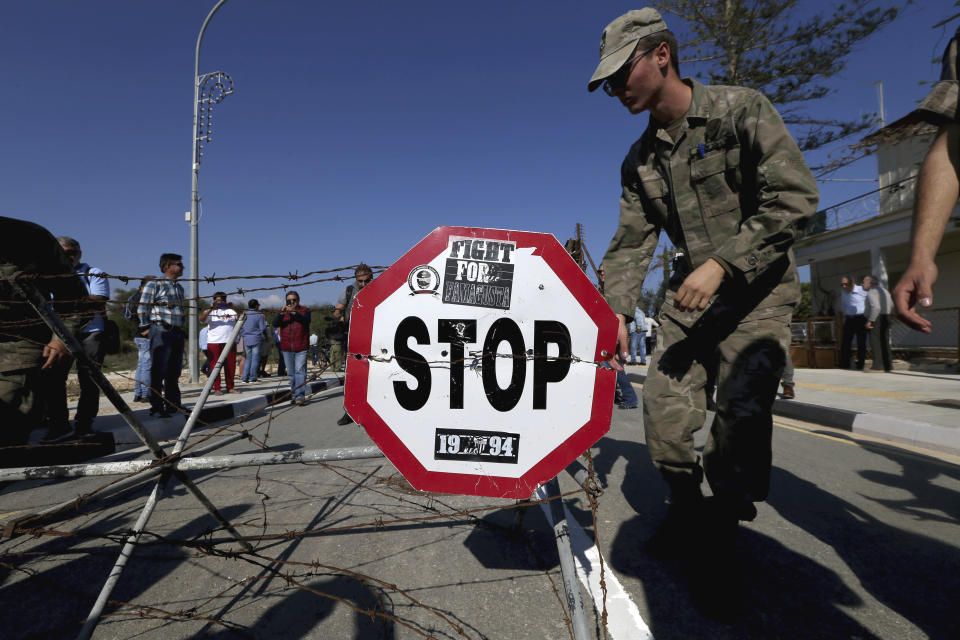 A Cypriot soldier removes the barbed-wire that blocked the road, at a newly-opened crossing point between ethnically split Cyprus' internationally recognized south and the breakaway, Turkish Cypriot north at the southeastern village of Dherynia on Monday, Nov. 12, 2018. A few hundred Greek Cypriots and Turkish Cypriots walked through a newly opened crossing point in the southeastern village of Dherynia in what peace activists are hailing as further breaking down barriers on ethnically divided Cyprus. (AP Photo/Petros Karadjias)