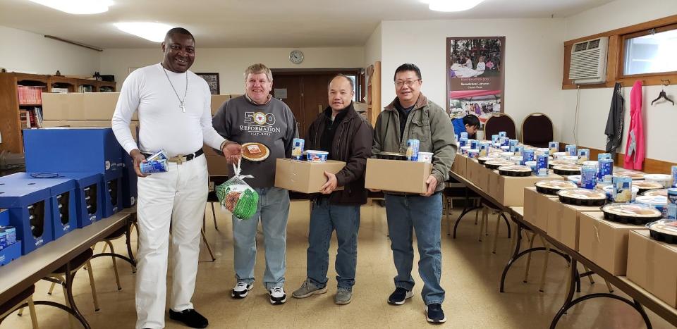 Kasongo Gui Kabeo, Don Hougard and Moua Vang, who lead congregations at Benediction Lutheran Church, carry boxes for a Thanksgiving dinner giveaway in 2021. They were joined by the church's first Hmong pastor, Blong Vang, right.