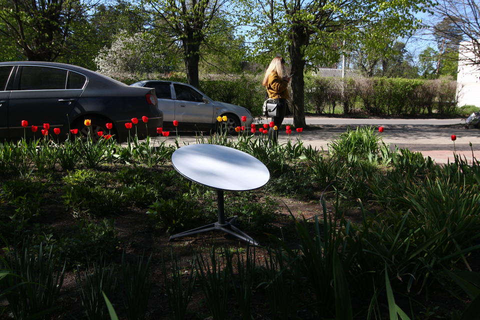 A person looks at a smartphone near a SpaceX Starlink internet terminal installed in a flower bed in Vorzel, Ukraine. 