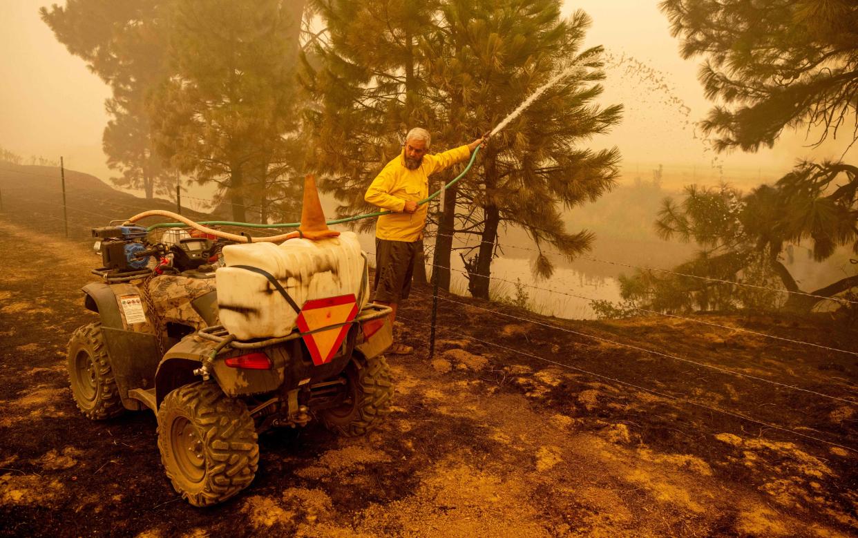 Volunteer firefighter Jarret LePage waters down a hot spot on his neighbor's property during the Dixie fire in Greenville, Calif. on Aug. 7, 2021. LePage helped protect both his and his neighbor's houses in Greenville.