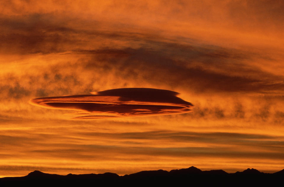 Lenticular clouds form a saucer shape in the orange glow of the sunset. Sumner Valley, Washington, USA.