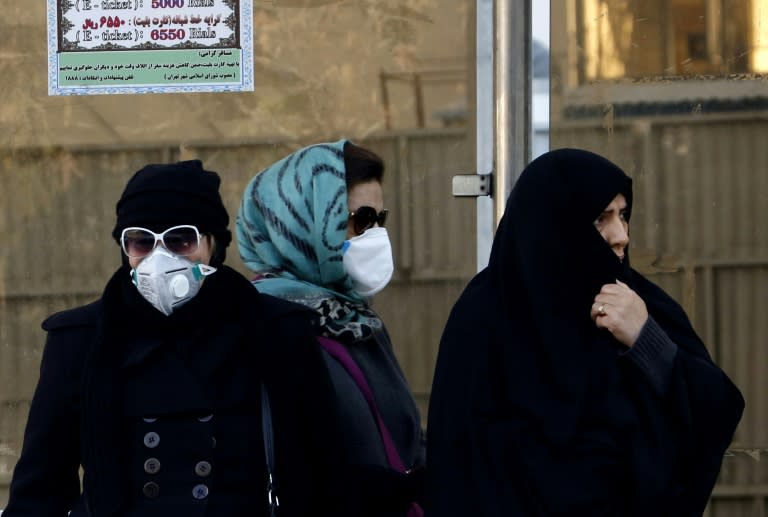 Iranian women wearing face masks wait at a bus stop in Tehran on December 17, 2017 after choking pollution blanketed the capital