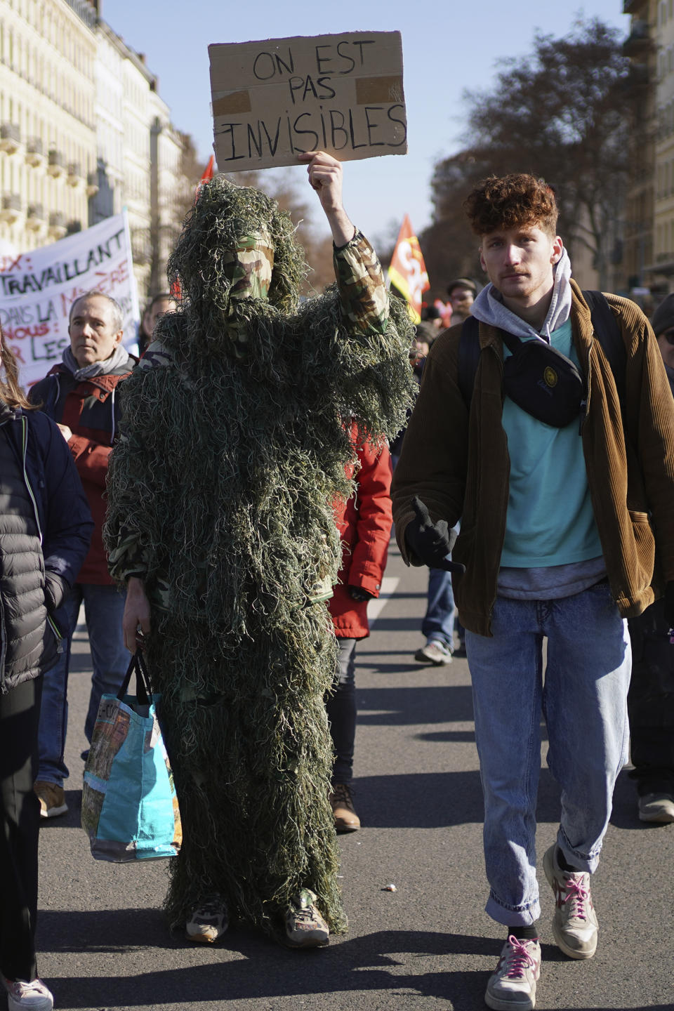 Demonstrators, one holding a placard reading "We are not Invisibles" during a march against pension reforms in Lyon, central France, Tuesday, Feb. 7, 2023. Public transportation, schools and electricity, oil and gas supplies were disrupted on Tuesday in France as demonstrators were taking to the streets for a third round of nationwide strikes and protests against the government's pension reform plans. (AP Photo/Laurent Cipriani)