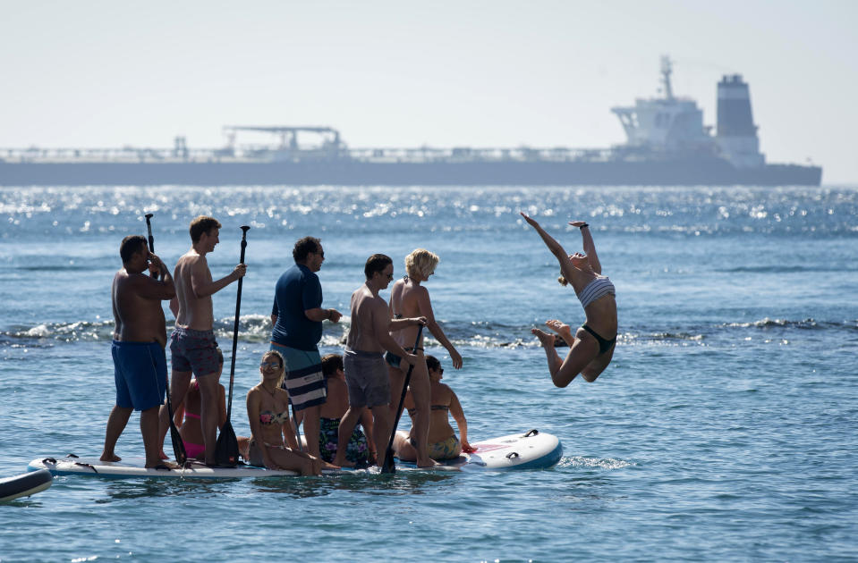 Renamed Adrian Aryra 1 super tanker is seen in background as people cool-off in the water in the British territory of Gibraltar, Sunday, Aug. 18, 2019. Authorities in Gibraltar on Sunday cleared the way for an Iranian supertanker to sail to an undisclosed location after rejecting the United States' latest request not to release the vessel. (AP Photo/Marcos Moreno)