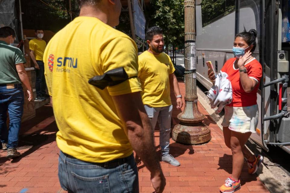 Orlando Andara, of Washington, front left, and Derick Alegria, center, both with the nonprofit SAMU First Response, greet people seeking asylum as a bus of asylum seekers who were sent from Arizona to Washington arrives, Thursday, Aug. 11, 2022, to a church on Capitol Hill in Washington. (AP Photo/Jacquelyn Martin)