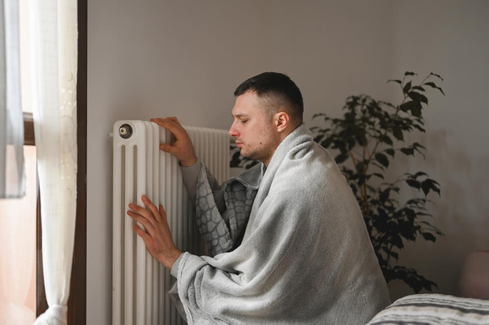 man covered in blanket and warming hands on a radiator