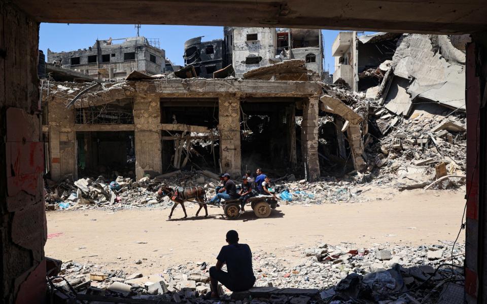 TOPSHOT - A man looks on as displaced Palestinians ride a donkey-pulled cart along a devastated street in Khan Yunis in the southern Gaza Strip on May 24, 2024, amid the ongoing conflict between Israel and Hamas. (Photo by Eyad BABA / AFP) (Photo by EYAD BABA/AFP via Getty Images)