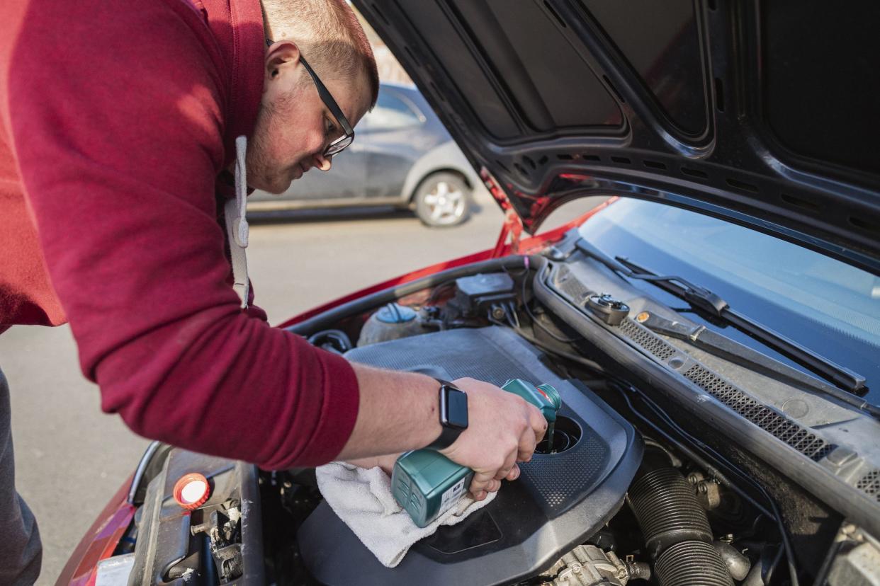 Young caucasian man adding oil to a car under the bonnet.