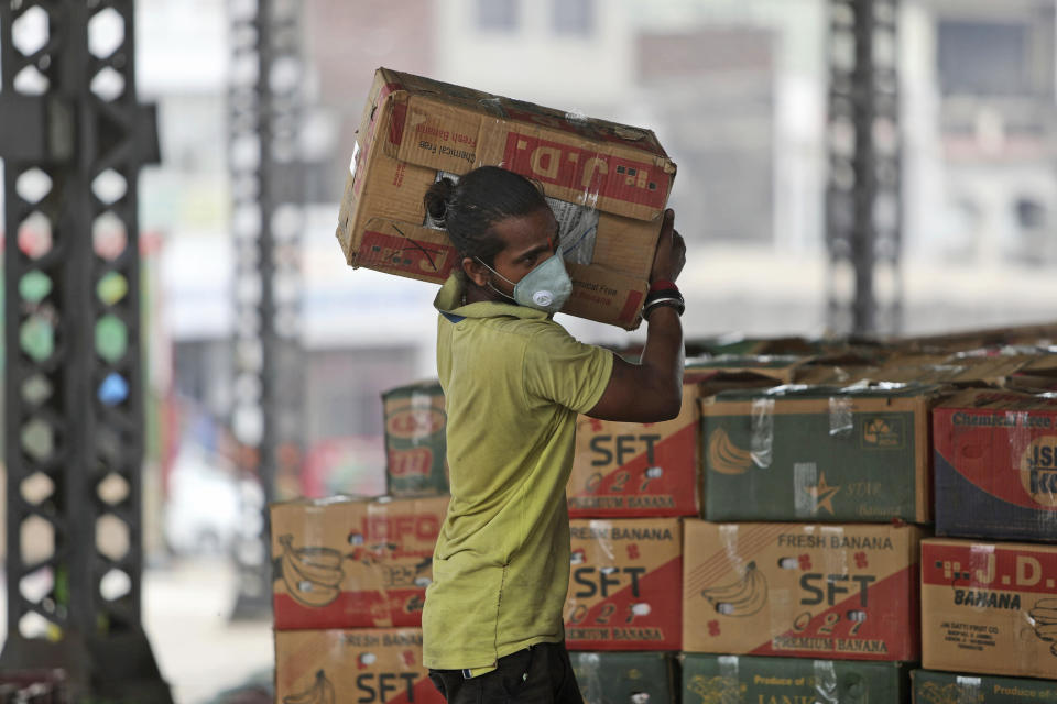 A man wearing a mask carries boxes of fruits at a market in Jammu, India, Tuesday, June 23, 2020. (AP Photo/Channi Anand)