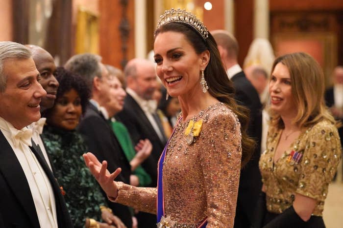 Kate Middleton, wearing a sequined gown and tiara, speaks with a line of elegantly dressed individuals at a formal event