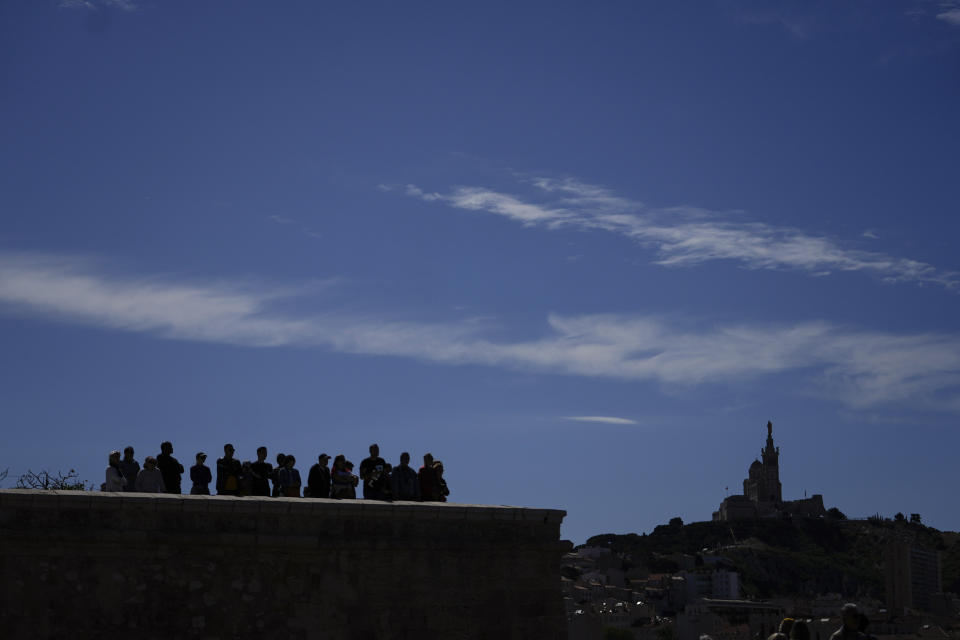 People wait from the Mucem museum view point ahead of the arrival of the Belem, the three-masted sailing ship which is carrying the Olympic flame, in Marseille, southern France, Wednesday, May 8, 2024. After leaving Marseille, a vast relay route is undertaken before the torch odyssey ends on July 27 in Paris. The Paris 2024 Olympic Games will run from July 26 to Aug.11, 2024. In background is Notre Dame de la Gard church. (AP Photo/Thibault Camus)