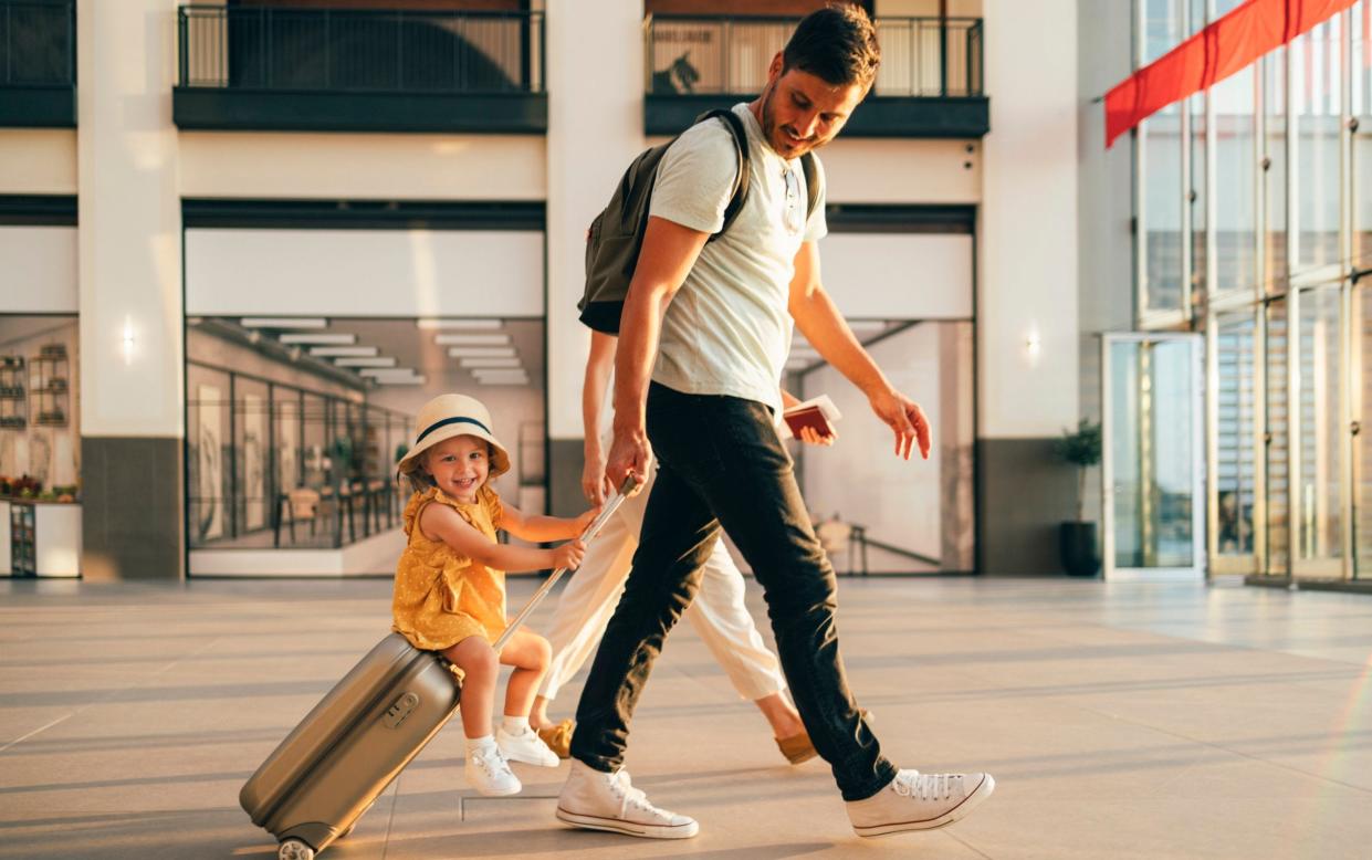 Cheerful husband and his anonymous wife walking with their little girl sitting on luggage at the airport