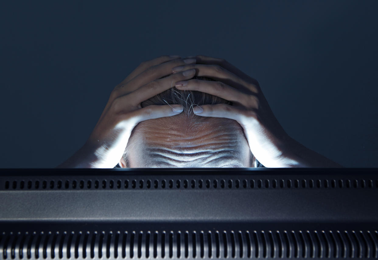 Top shot of distressed man with both hands over his head staring into a computer screen.