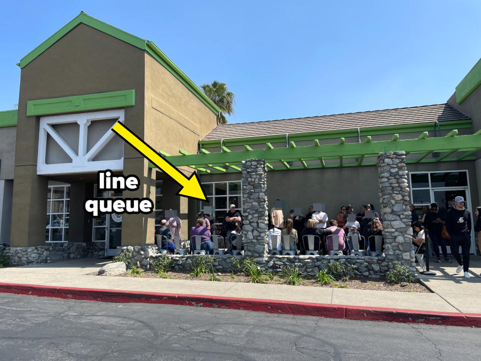 People waiting outside a restaurant with stone pillars and green trim