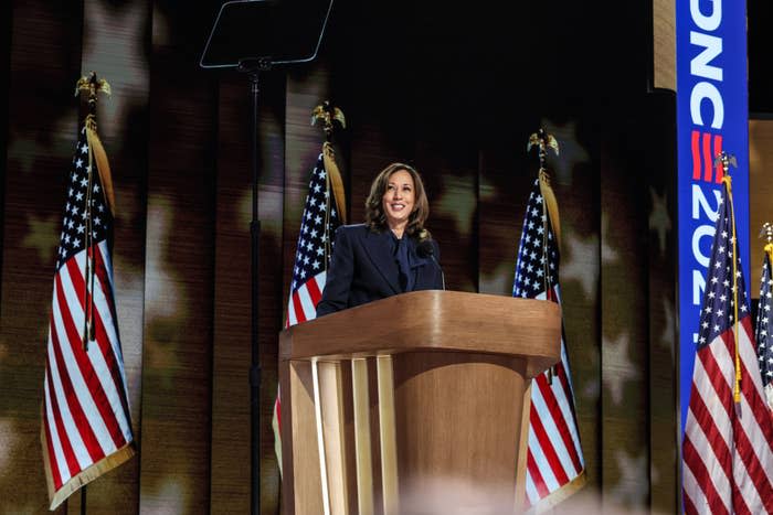 Kamala Harris stands at a lectern with American flags in the background and gives a speech. A teleprompter screen can be seen above her