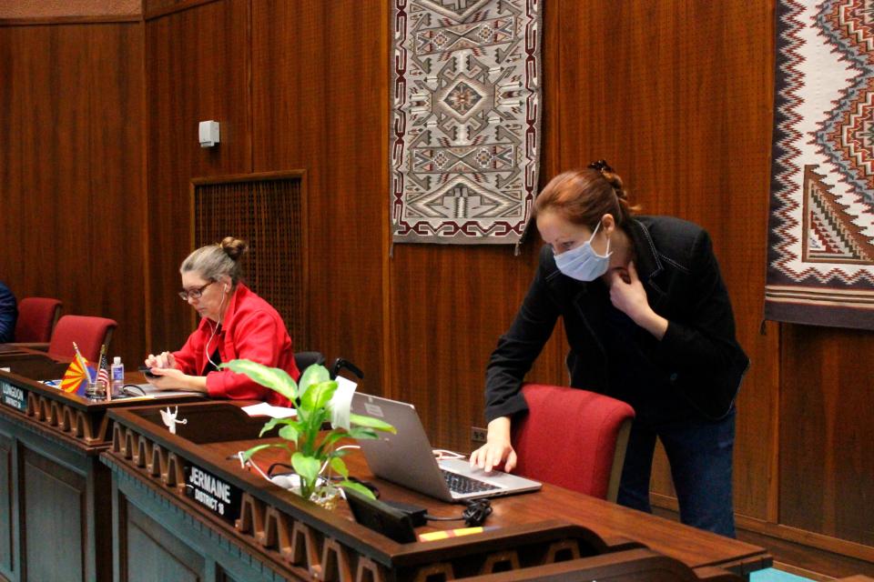 State Rep. Jennifer Jermaine, wearing a mask, looks at documents on her computer as fellow Democratic Rep. Jennifer Longdon, left, looks at her phone before the start of an unusual floor session at the Arizona House in Phoenix, on Thursday, March 19, 2020.