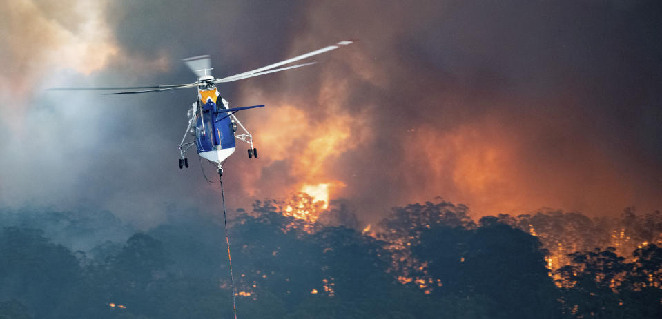 In this Monday, Dec. 30, 2019 photo provided by State Government of Victoria, a helicopter tackles a wildfire in East Gippsland, Victoria state, Australia. Wildfires burning across Australia's two most-populous states trapped residents of a seaside town in apocalyptic conditions Tuesday, Dec. 31, and were feared to have destroyed many properties and caused fatalities. (State Government of Victoria via AP)