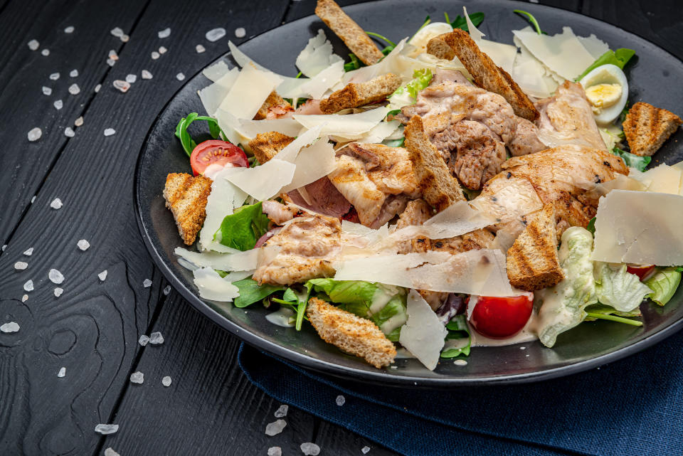 Fresh caesar salad in white plate on dark wooden table. Top view. Photo for the menu