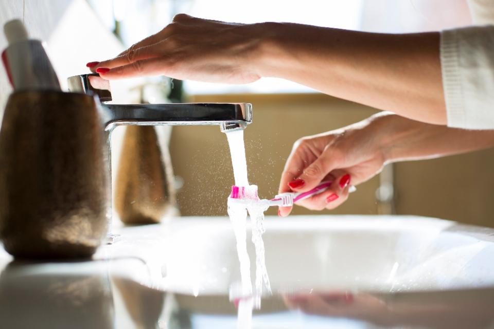 Woman rinsing her toothbrush, close-up of hands (How to clean a toothbrush)