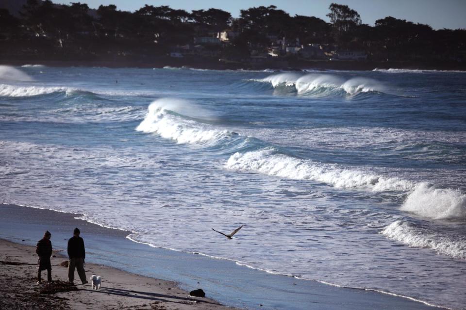 A couple walk the beach during high tide in Carmel-by-the-Sea.