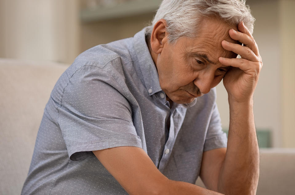 A concerned looking senior man hunches over and holds his head