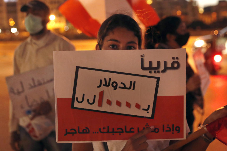 A protester holds an Arabic placard that reads: "Soon $ 1 = 10,000 Lebanese pounds and if you are not happy, immigrate," during a protest against the economic and financial crisis, in front of the government house in downtown Beirut, Lebanon, Thursday, June 11, 2020. The Lebanese pound has hit a record low against the dollar on the black market as the country's political crisis deepens and foreign currency reserves dwindle further. (AP Photo / Hussein Malla)