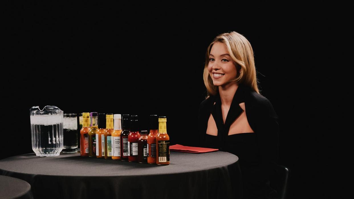sydney sweeney sitting at a table with a lot of hot sauce on it