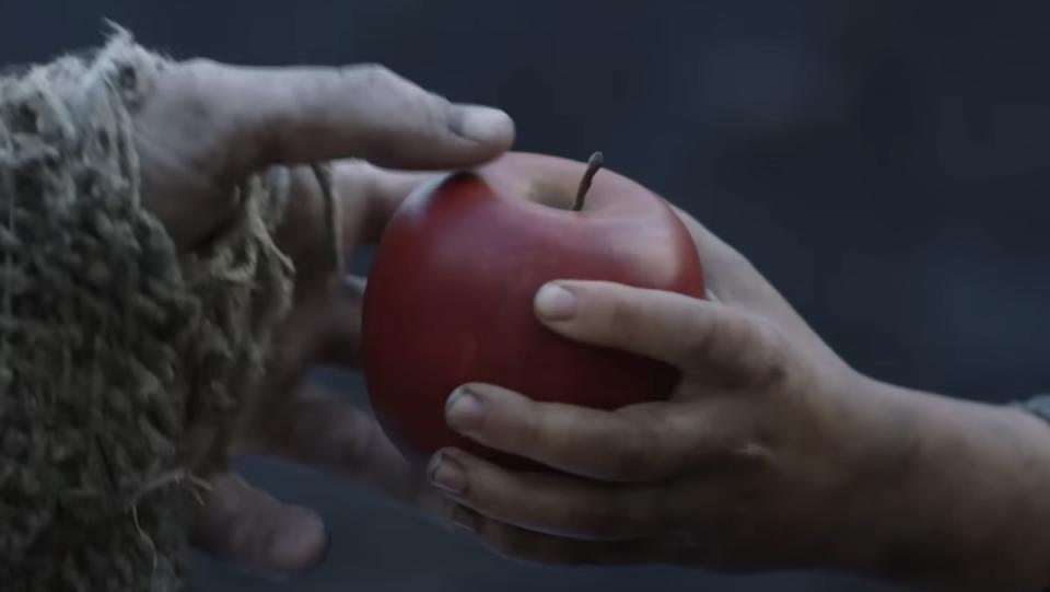 The hand of Nori giving an apple to the hand of The Stranger on The Rings of Power
