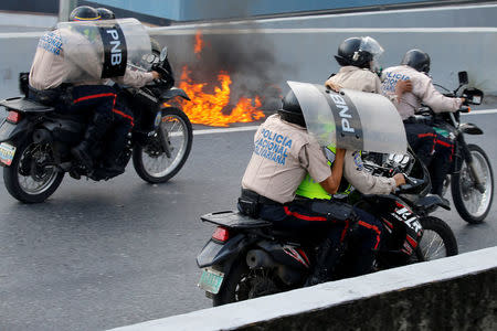 Riot police officers on motorcycles shield themselves during clashes with opposition supporters while rallying against Venezuela's President Nicolas Maduro in Caracas. REUTERS/Carlos Garcia Rawlins