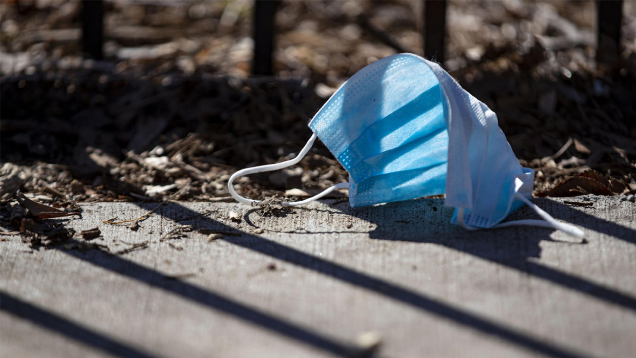 A surgical mask lies discarded on the sidewalk. 