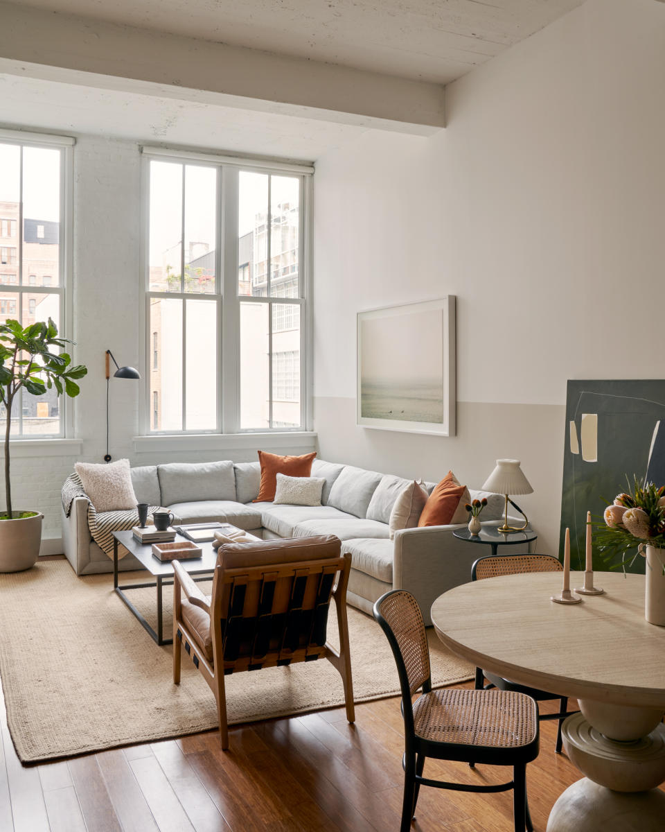 Living-dining room with neutral walls, L-shaped sofa, armchair and coffee table on top of rug, and round dining table in foreground