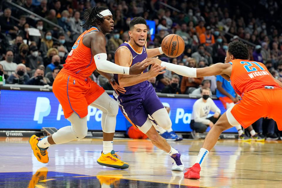 Phoenix's Devin Booker (center) tries to slip between Oklahoma City's Lu Dort (left) and Aaron Wiggins during Wednesday night's NBA game at Footprint Center.