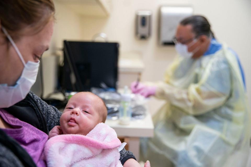 sick baby being held by mom in face mask at clinic