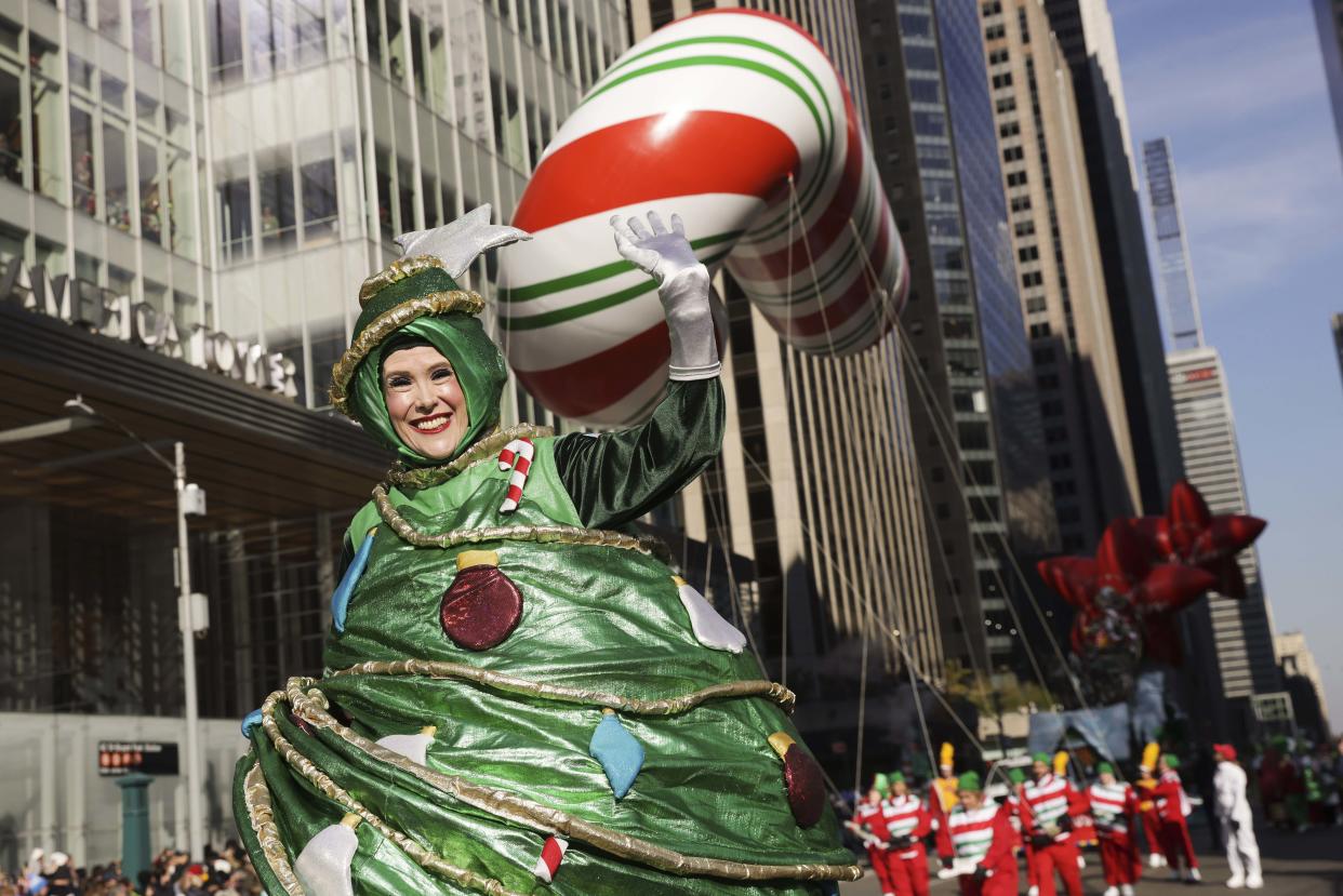 A parade performer in a Christmas Tree leads a giant candy cane down Sixth avenue.  (Jeenah Moon / AP)