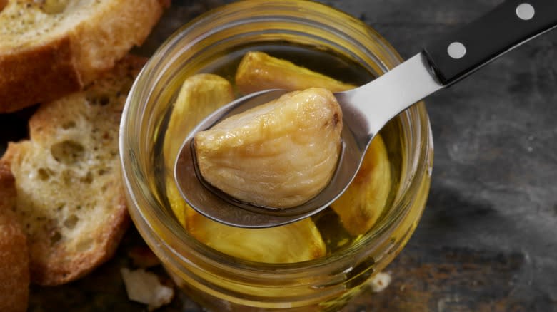 spoon pulling confit garlic from jar