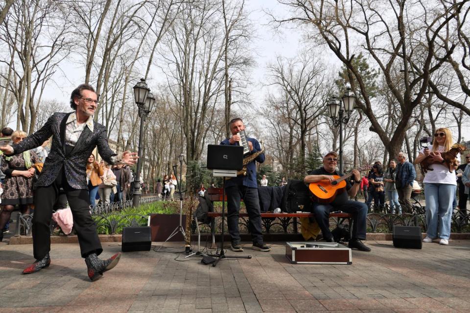 A man dances on a brick path as musicians play.