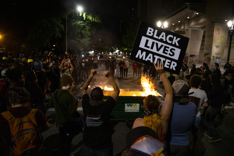 CORRECTS DAY AND DATE TO FRIDAY JULY 10. - FILE - In this Friday, July 10, 2020 file photo, a waste receptacle's contents are in flames as protesters gather in downtown Portland, Ore. The mayor of Portland, Oregon said late Sunday the U.S. Marshals Service are investigating the injury of a protester who was hospitalized in critical condition over the weekend after being hit in the head by an impact weapon fired by a federal law enforcement officer. Mayor Ted Wheeler said he spoke with with U.S. Attorney for Oregon Billy J. Williams and learned of the investigation. (Dave Killen/The Oregonian via AP, File)