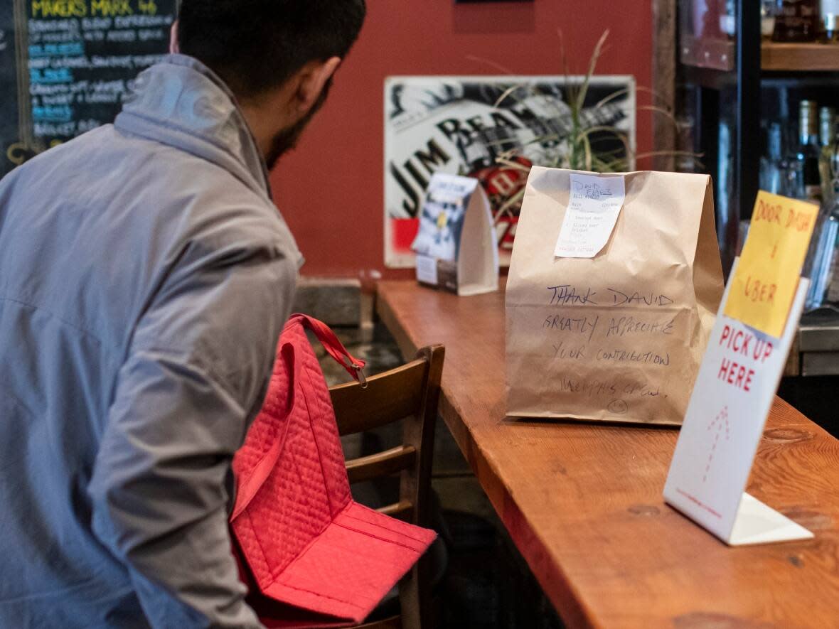 George Siu of Memphis Blues BBQ hands an order to a delivery driver at his restaurant in Vancouver. Last week, the province introduced legislation that would cap the fees that service delivery companies like Door Dash charge to restaurants. (Ben Nelms/CBC - image credit)
