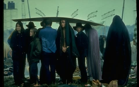 Students draped in blankets huddled under sheet of cardboard in rain at Woodstock music festival - Credit: John Dominis/Getty