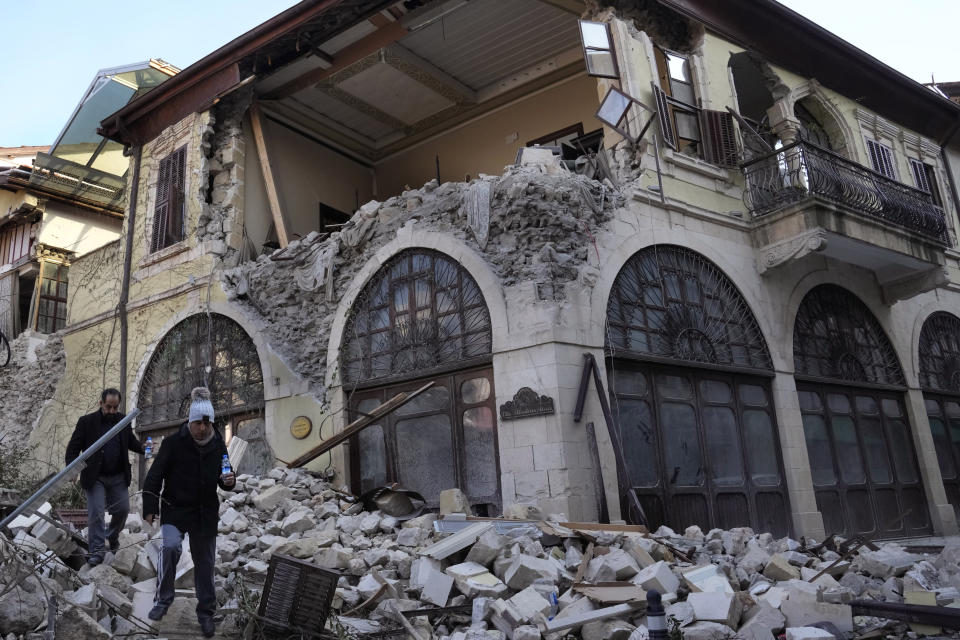 Turkish citizens pass in front of a heritage hotel that destroyed during the devastated earthquake, in the old city of Antakya, southern Turkey, Monday, Feb. 13, 2023. Antakya, known as Antioch in ancient times, has been destroyed many times by earthquakes. It was destroyed yet again by an earthquake earlier this month, and residents are wondering if its ancient glories will ever come back. (AP Photo/Hussein Malla)