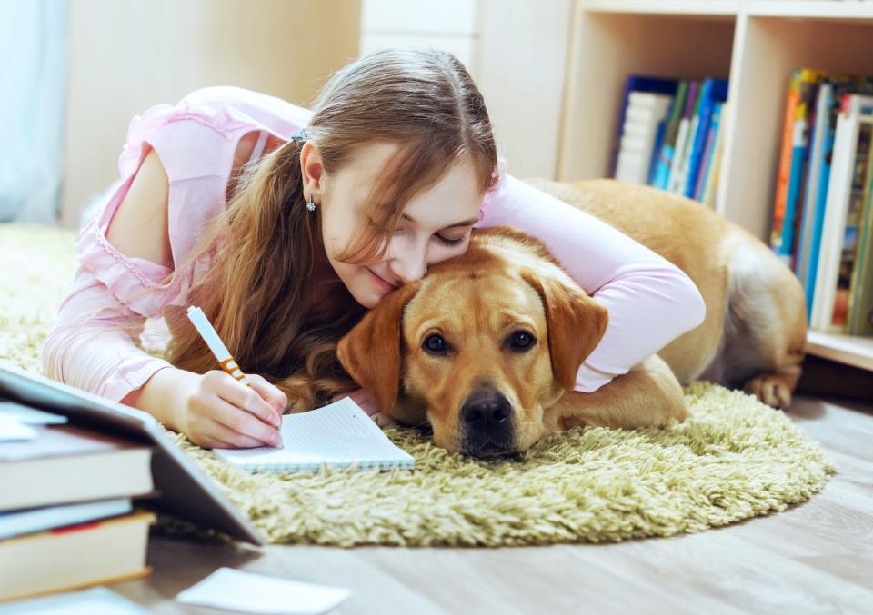 A student lying on the floor cuddles up with her dog as she takes notes