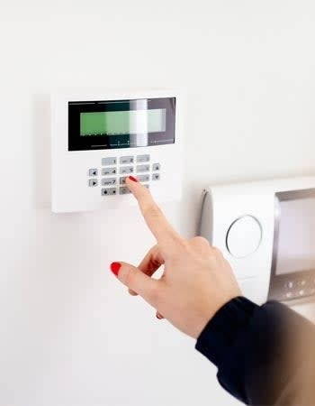 A close up of a woman's hand pressing buttons on a wall-mounted home security system.