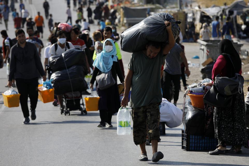 Migrants carry their belongings as they flee a road leading from Moria to the capital of Mytilene, on the northeastern island of Lesbos, Greece, Thursday, Sept. 17, 2020. A Greek police operation is underway on the island of Lesbos to move thousands of migrants and refugees left homeless after a fire destroyed their overcrowded camp, into a new facility on the island. (AP Photo/Petros Giannakouris)