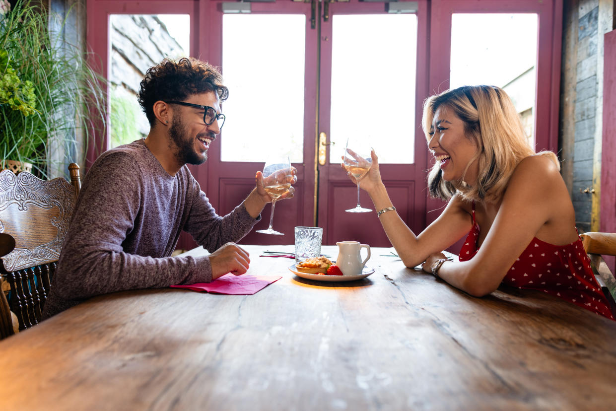 Side view in a cozy bar, a well-dressed couple shares a date night to remember. They are laughing and enjoying glasses of white wine, their connection radiates warmth and joy.