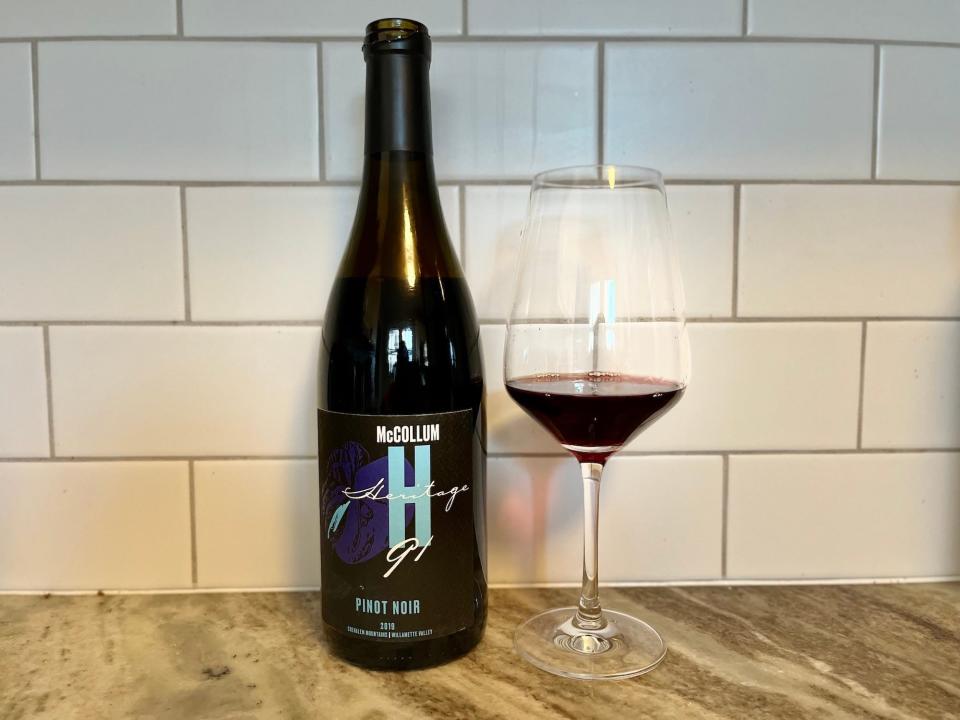 A bottle of McCollum Heritage 91 Pinot Noir sits on a counter next to a small glass of the wine.