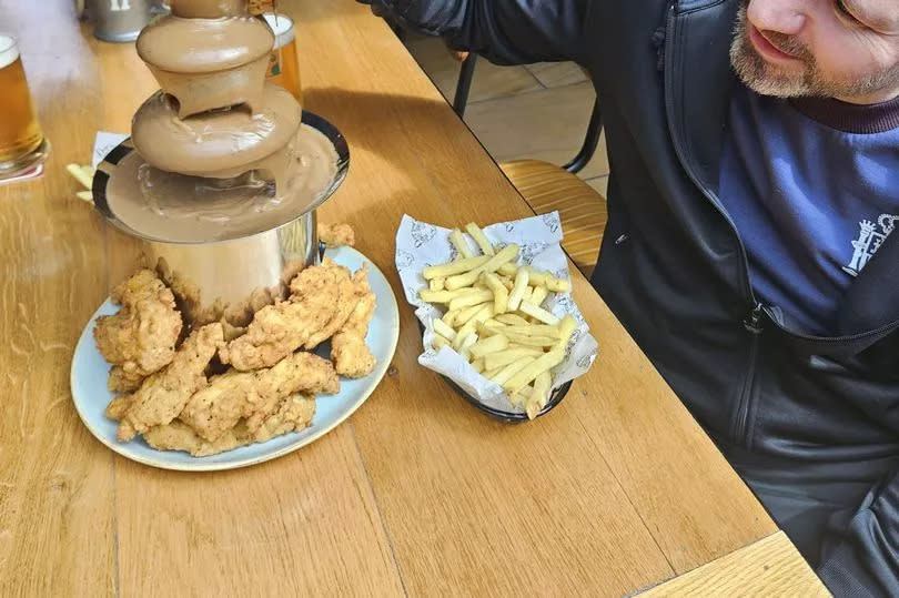 A man dipping a fried chicken leg into a gravy fountain